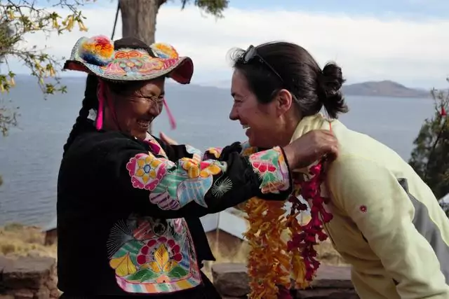 Une péruvienne enfilant un collier de fleur au cou d'une touriste