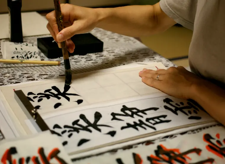 Un individu pratique la calligraphie en traçant des kanjis sur du papier avec un pinceau.