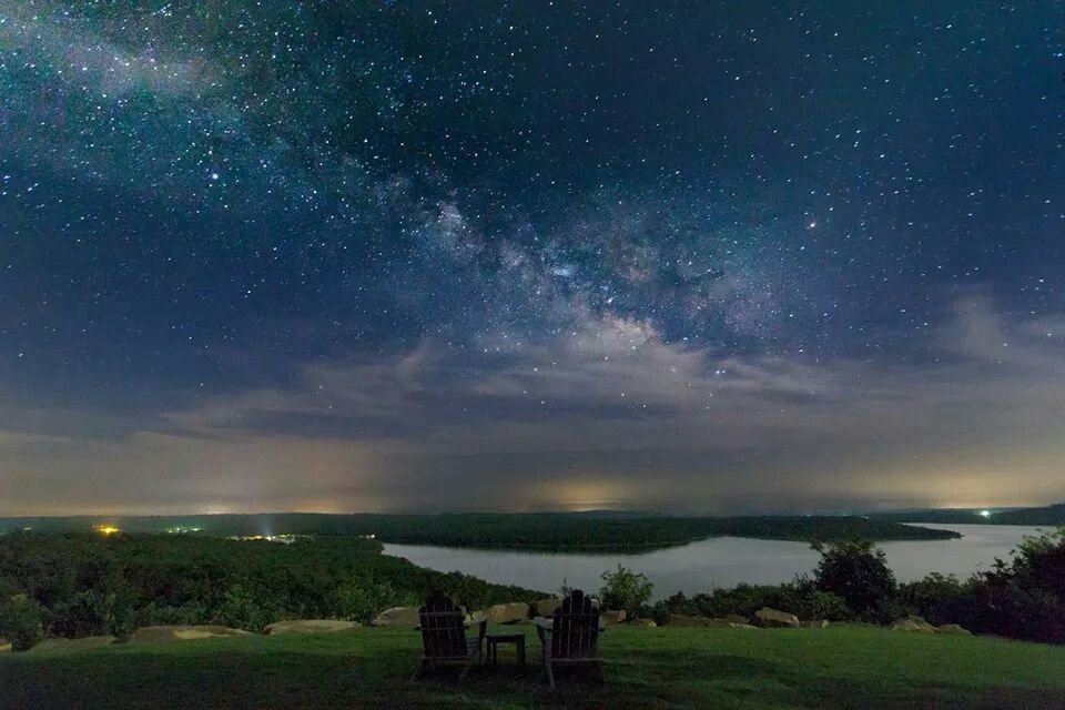 La Voie lactée illumine le ciel nocturne au-dessus d'un lac paisible, créant une scène magique avec deux fauteuil appelant à faire une pause.