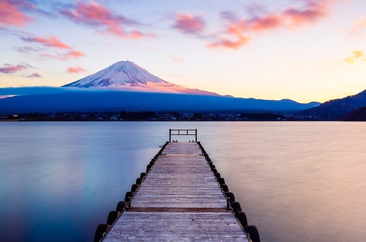 Un quai en bois s'étend dans l'eau au coucher du soleil, avec le mont Fuji en arrière-plan.